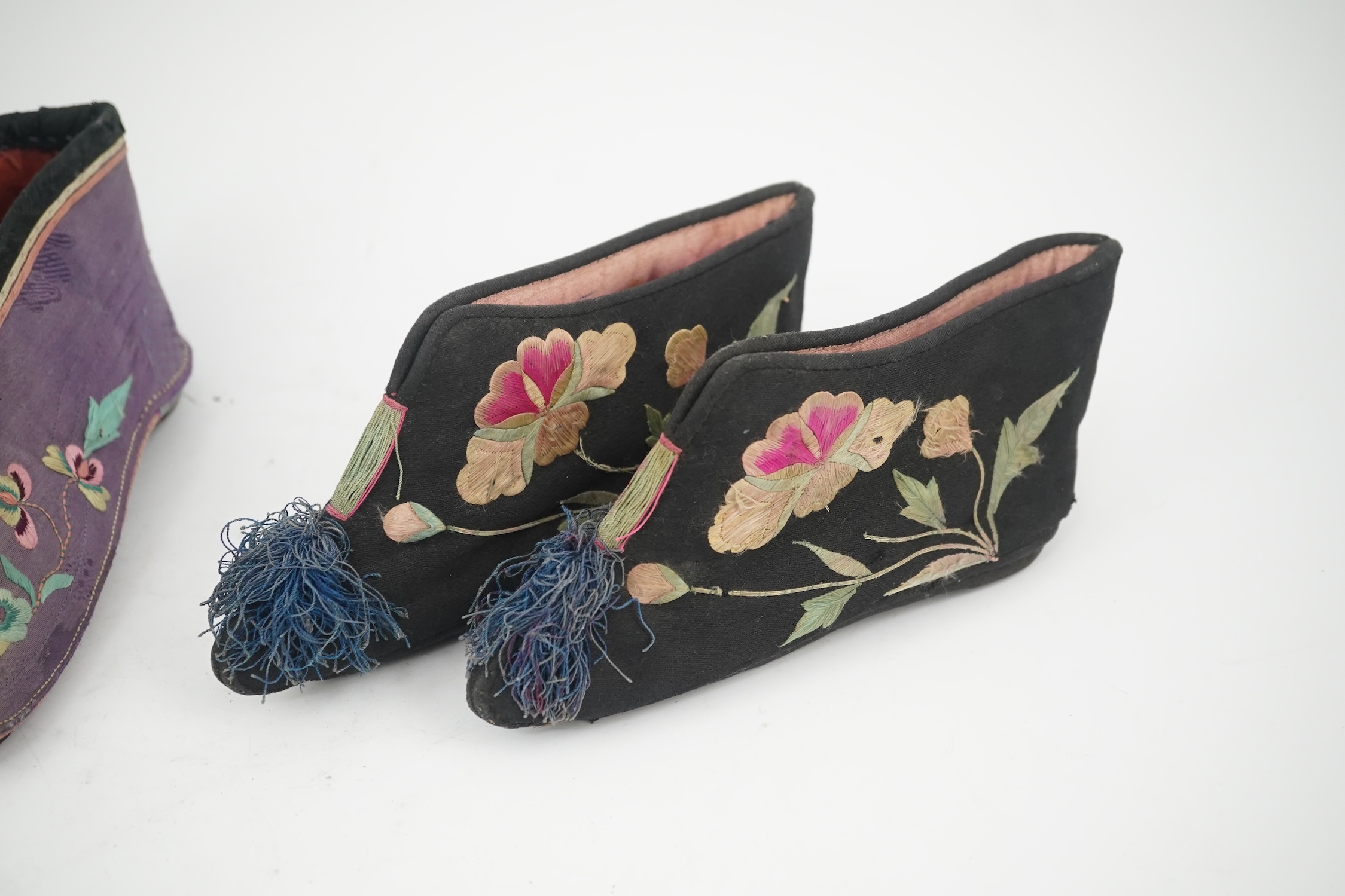 Four pairs of late 19th / early 20th Chinese ladies bound foot shoes, made in various coloured silks, with colourful floral embroidered motifs, two pairs with decorative silk pom-poms and another made of purple and black